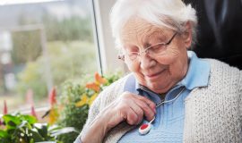 Elderly lady sat at home admiring her personal alarm pendant hanging from her neck