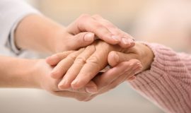 Nurse holding hands of elderly woman against blurred background